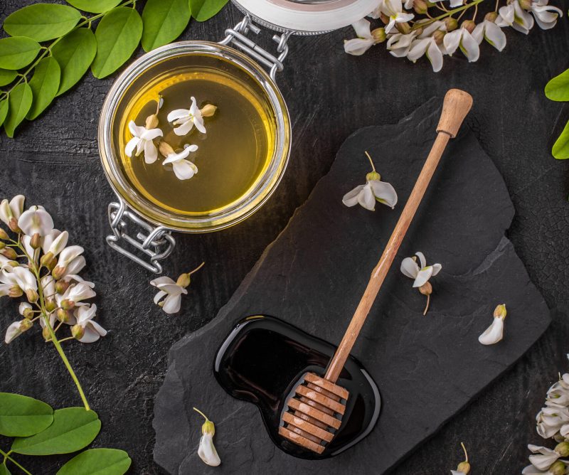 Composition with honey, acacia flowers and honey dipper on black background
