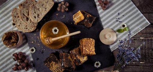 top view of fresh honey in glass jar, homemade bread and honeycombs on rustic table